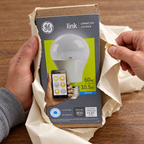 GE Link A19 daylight LED bulb carton in gift unwrapping setting; AI-generated lifestyle illustration