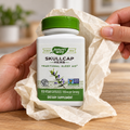 AI-generated illustration of adult hands unwrapping plain tissue from a closed Nature’s Way Skullcap Herb bottle labeled 100 vegan capsules and 850 mg per serving.