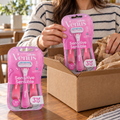 An adult unpacks two pink Gillette Venus Sensitive three-count razor packs from a shipping box, six razors total.