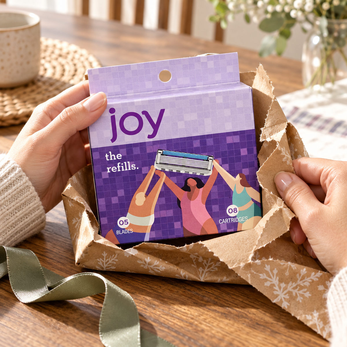 Adult hands pull gift wrap away from one joy refill box labeled 05 blades and 08 cartridges.