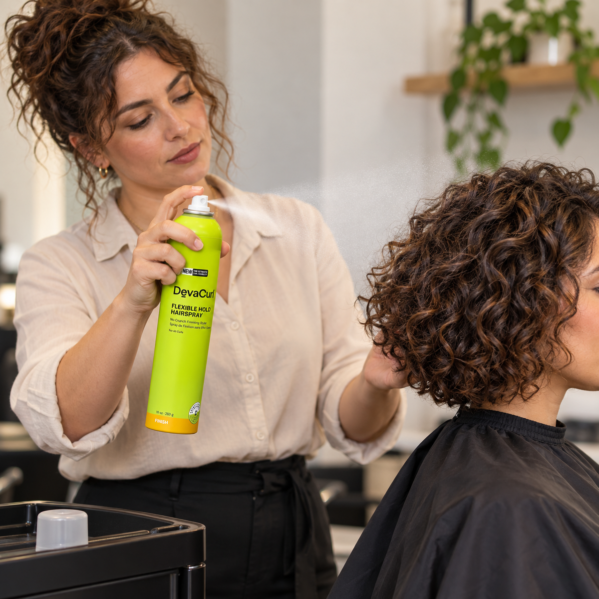 Stylist applying DevaCurl Flexible Hold Hairspray to the back of an adult client’s dry curls