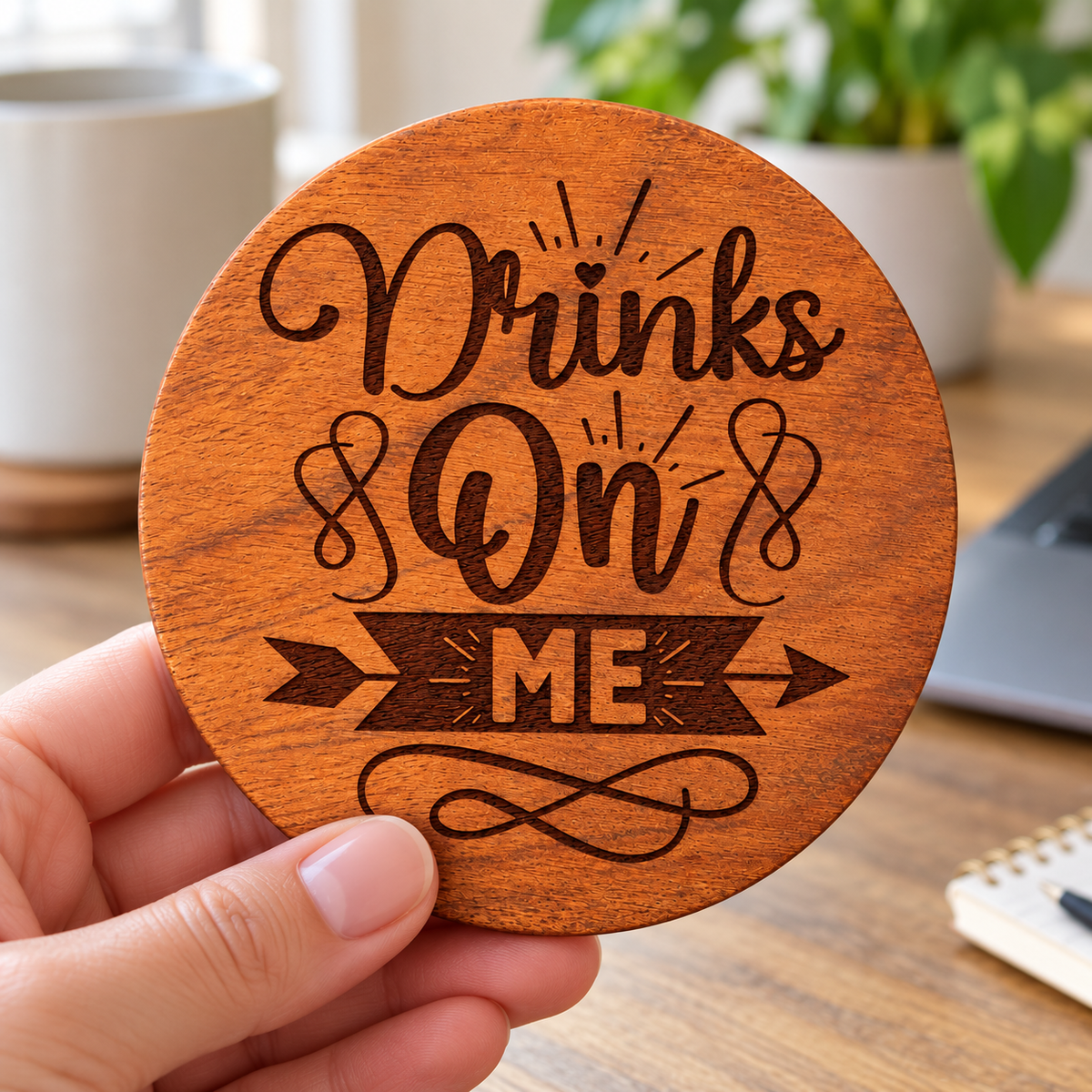 A hand holding one round Drinks On ME engraved wood coaster with the front design visible.