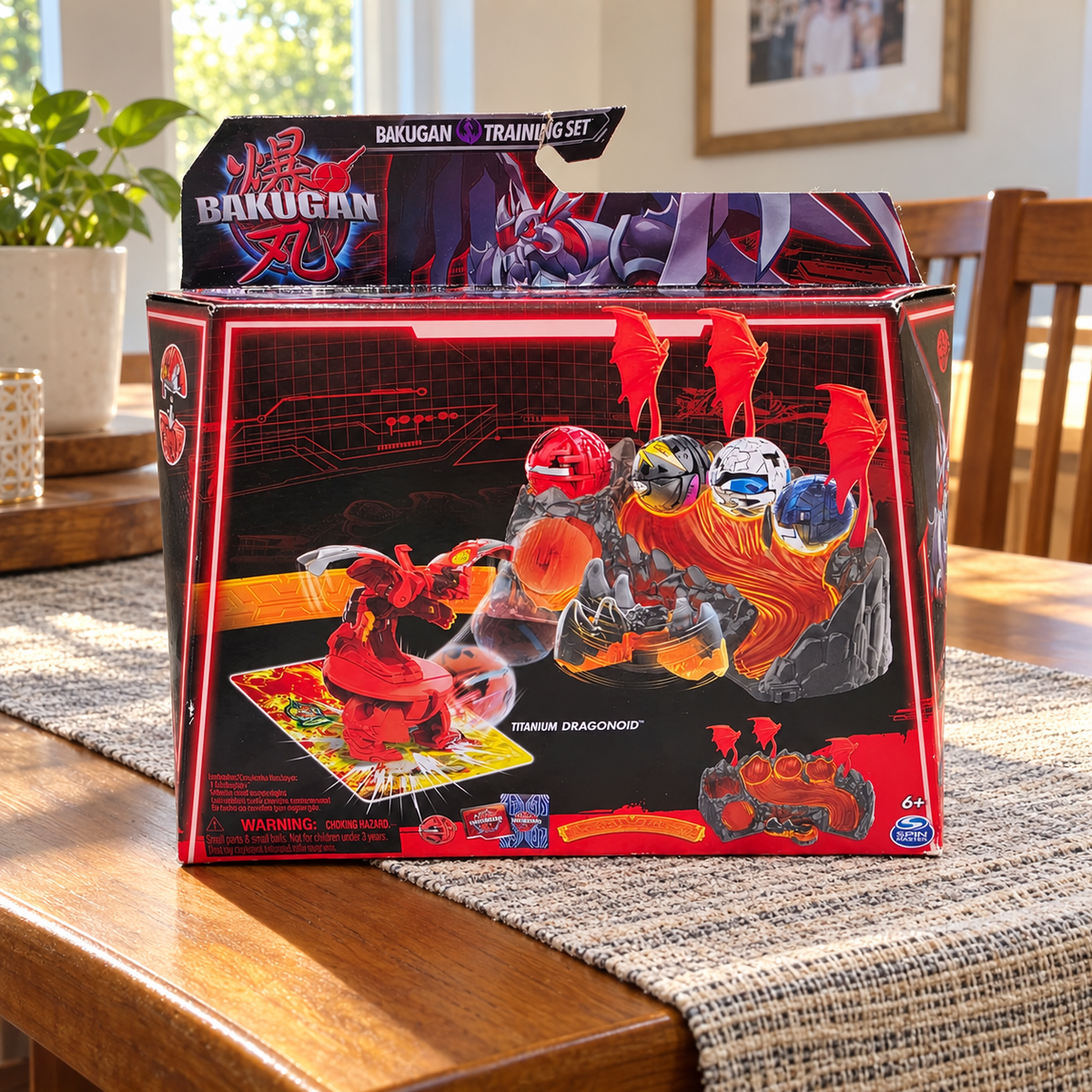 AI-generated context: pictured Bakugan Titanium Dragonoid Training Set retail carton with creases and edge wear on a dining table in a family home; room props not included, extra figures printed on carton are not additional included toys.