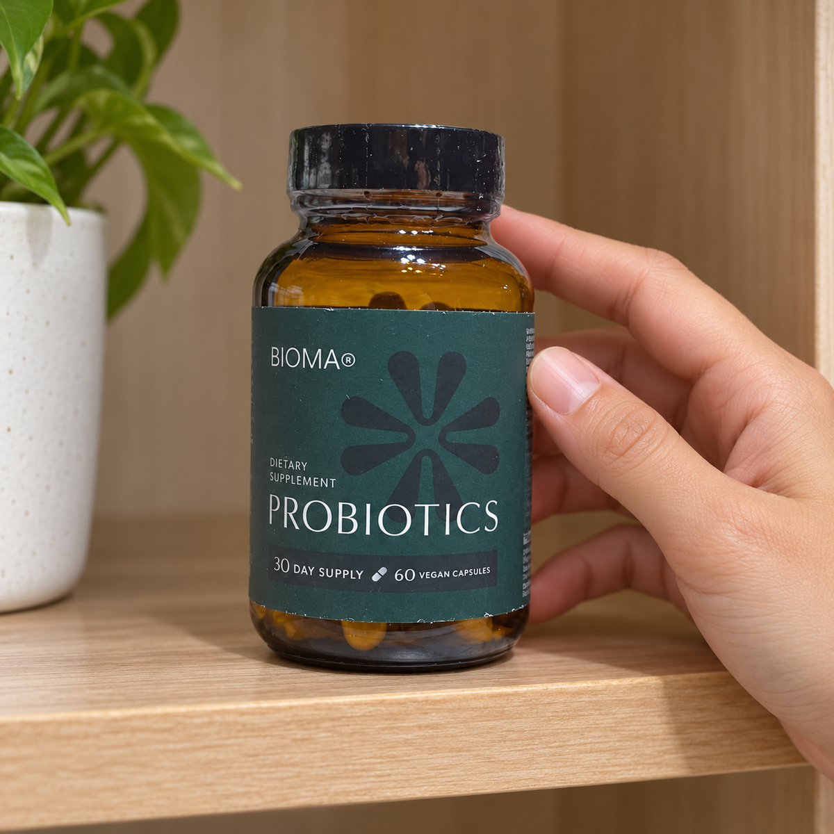 AI-generated lifestyle illustration of one matching teal-label BIOMA Probiotics 60-vegan-capsule bottle on a cupboard shelf beside a hand; props excluded.