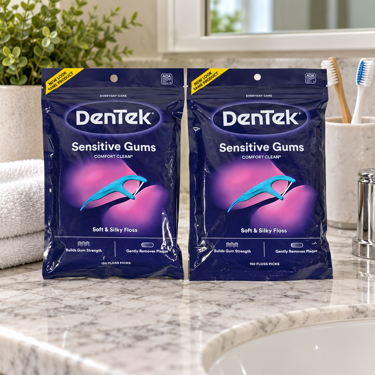AI-generated lifestyle illustration of exactly two DenTek Sensitive Gums Comfort Clean 150-count bags on a bathroom vanity beside a hand towel and toothbrush cup; setting props are not included.
