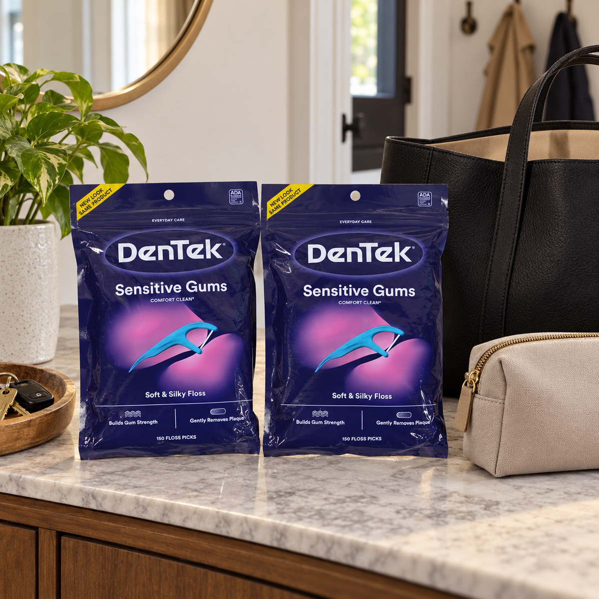 AI-generated lifestyle illustration of exactly two DenTek Sensitive Gums Comfort Clean 150-count bags on a entry console beside a work tote and personal-care pouch; setting props are not included.