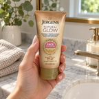 An adult holding a Jergens Natural Glow Face SPF 20 Fair to Medium tube beside a bathroom sink