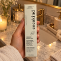 An adult holding a Cocokind Beginner Retinol Gel carton at an evening bathroom vanity