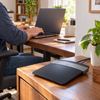 Working at a laptop with a Cisco Linksys E2500 router on a nearby desk. AI-assisted illustration.