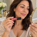 Holding a capped Pink Luster lip gloss while looking in a mirror
