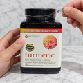 AI-generated preparation illustration of adult hands peeling the printed clear outer band from a Youtheory Turmeric Extra Strength 150-capsule bottle. Black cap remains closed.