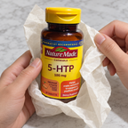 AI-generated illustration of adult hands unwrapping tissue from a closed Nature Made 5-HTP 100 mg orange citrus 30-tablet bottle.