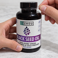 Hands removing the cap wrapping from a Zhou Black Seed Oil bottle.