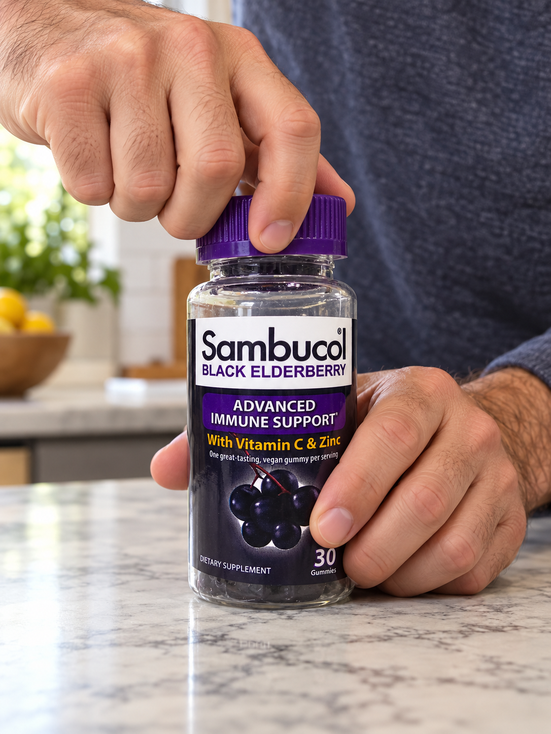 Hands opening a Sambucol Black Elderberry gummy bottle.