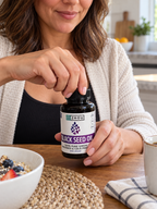 Hands opening a Zhou Black Seed Oil capsule bottle.