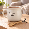 Cream Cocoa cutie mug filled with cocoa beside its wooden spoon on a cozy living-room table.
