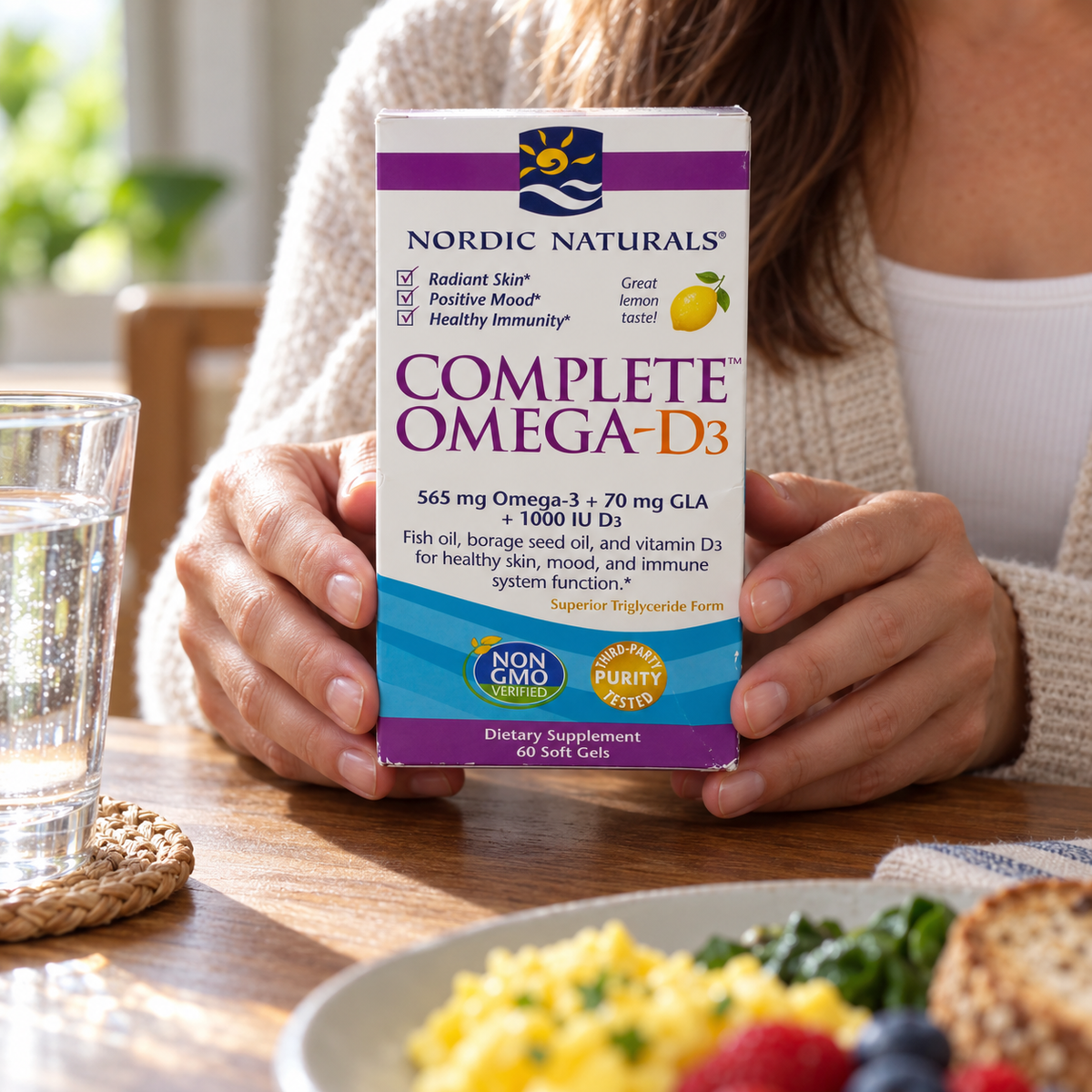 An adult holding the Nordic Naturals Complete Omega-D3 60-soft-gel box at a breakfast table