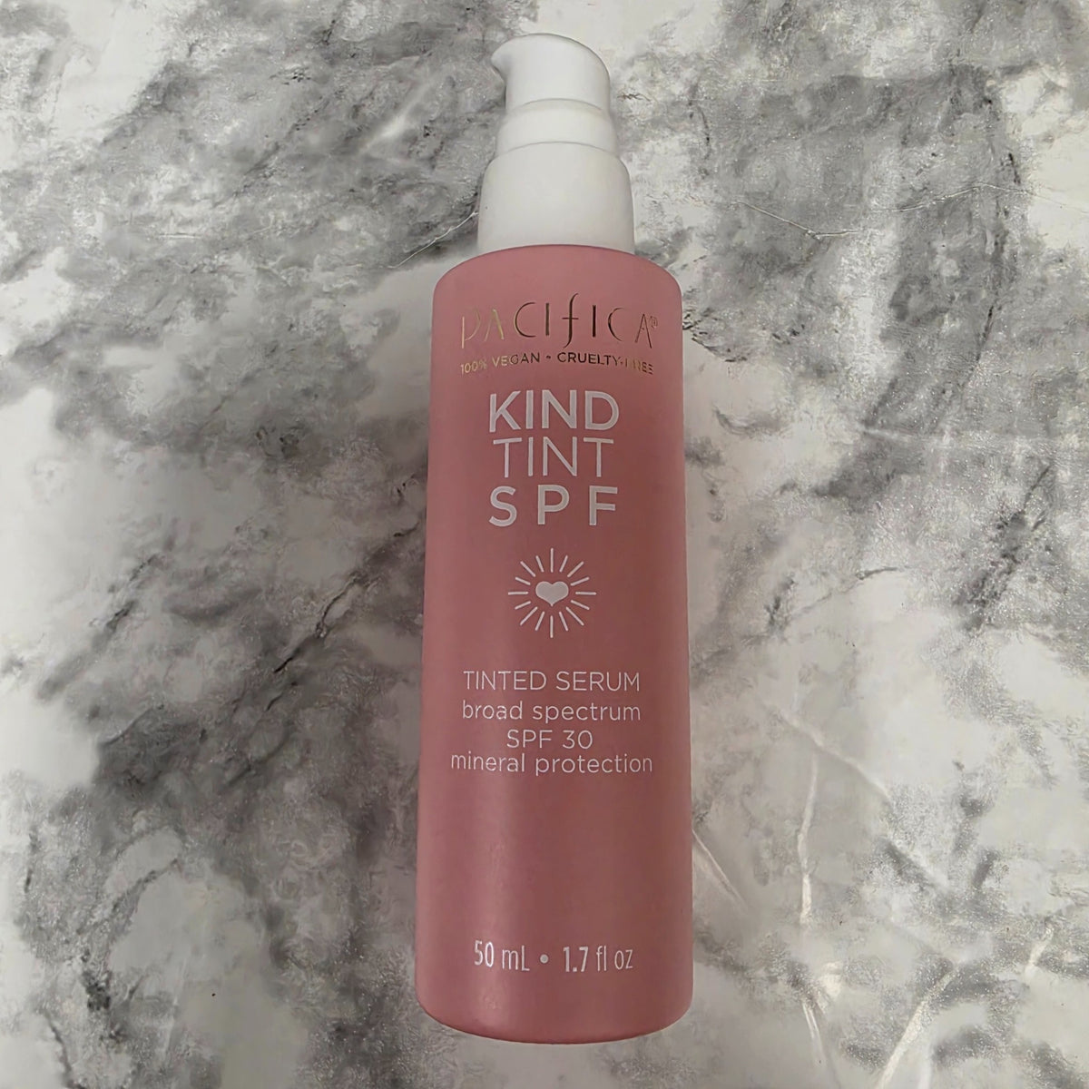 Pacifica Kind Tint SPF 30 tinted serum, 1.7 fl oz pink pump bottle on a marble background.