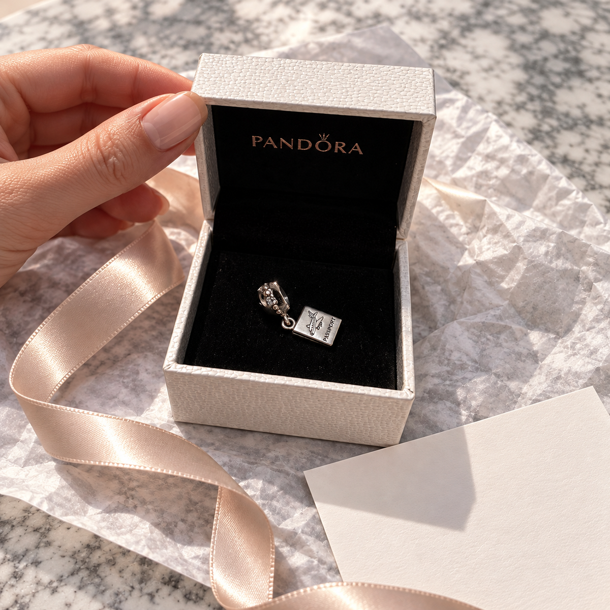 Passport charm presented in its white Pandora box beside a blank gift card