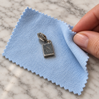 Crown-O reverse of the silver passport charm resting on a soft polishing cloth