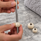 Close view of hands holding the threaded ball rod and pivot ball, with two spare ball sizes nearby.