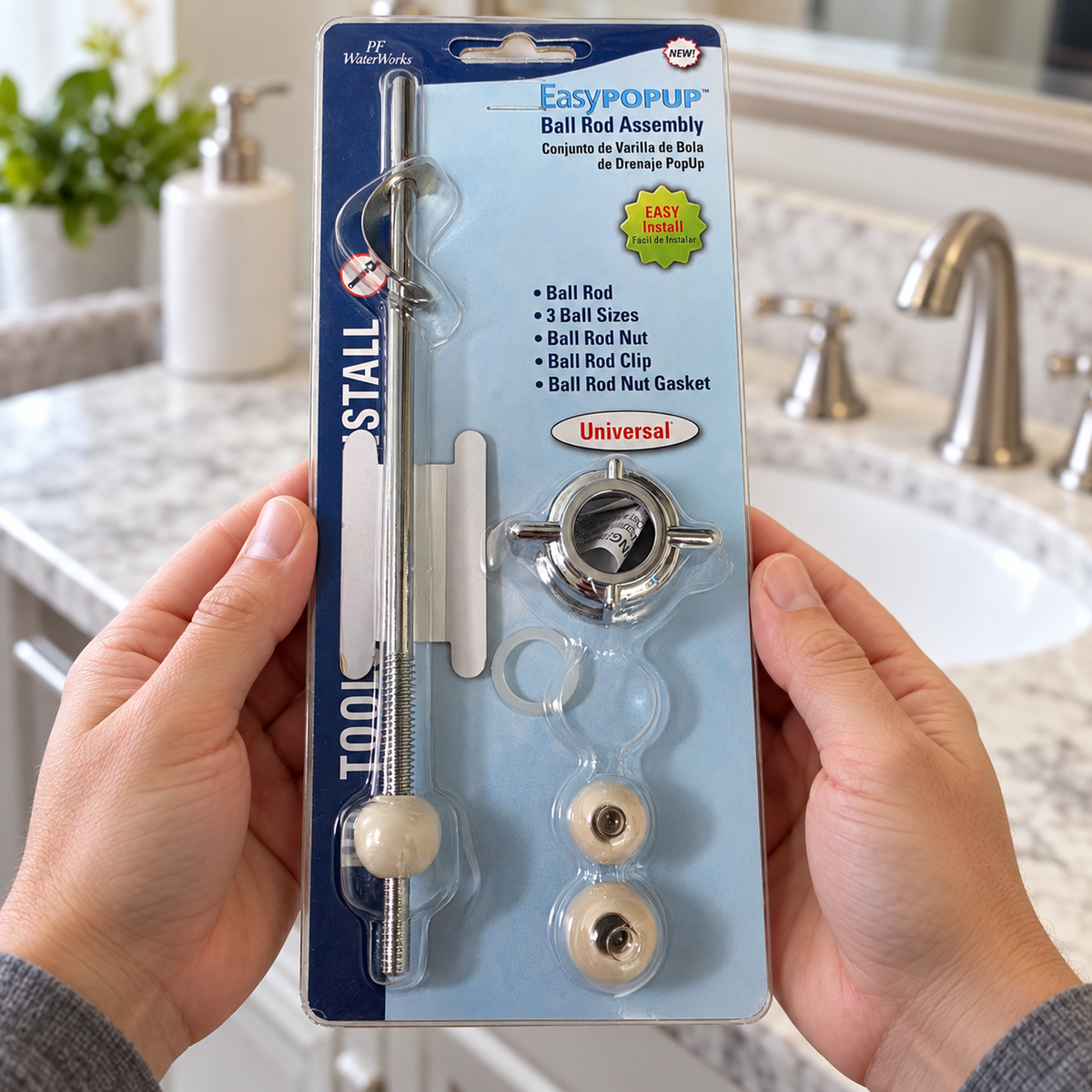 Hands holding the packaged EasyPOPUP PF0905 ball rod assembly in front of a bathroom vanity.