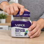 An adult beginning to unscrew the purple cap of a Natrol Melatonin MAX 10 mg Blueberry 32 Gummies bottle.