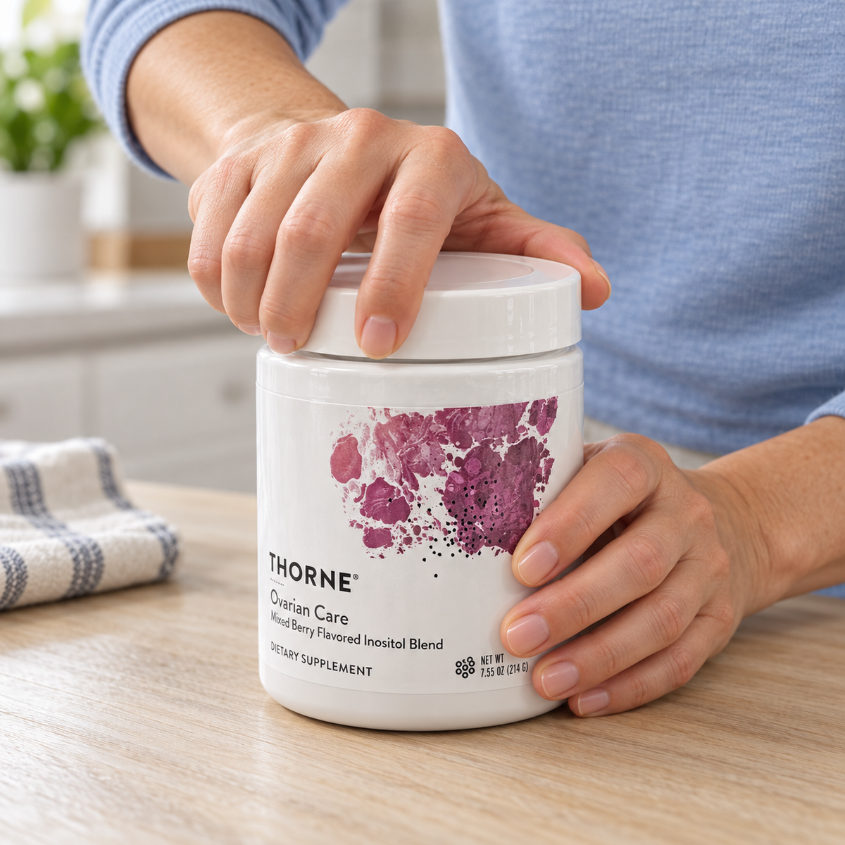 An adult beginning to unscrew the white lid of a Thorne Ovarian Care Mixed Berry 7.55 oz container.