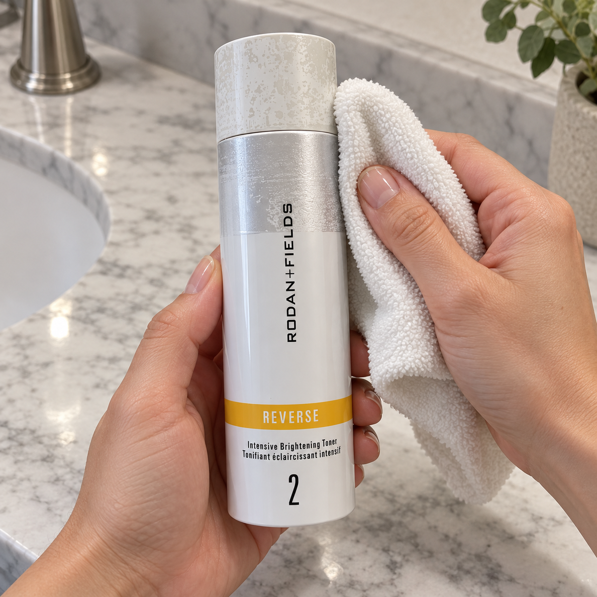 Wiping the outside of a capped Rodan + Fields REVERSE toner bottle with a soft cloth