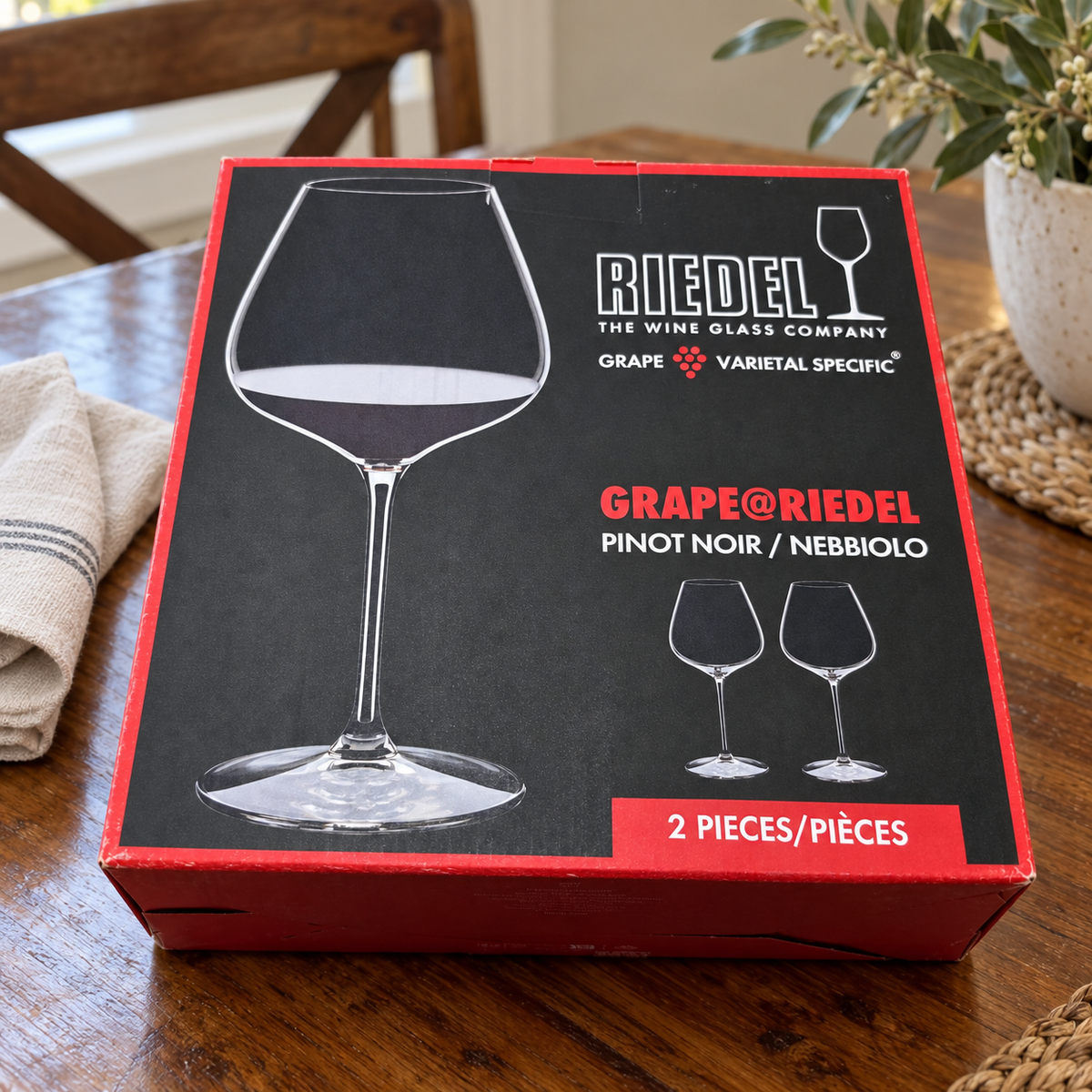 AI-generated lifestyle scene of one closed GRAPE@RIEDEL Pinot Noir Nebbiolo two-piece box on a dining table. Props not included.