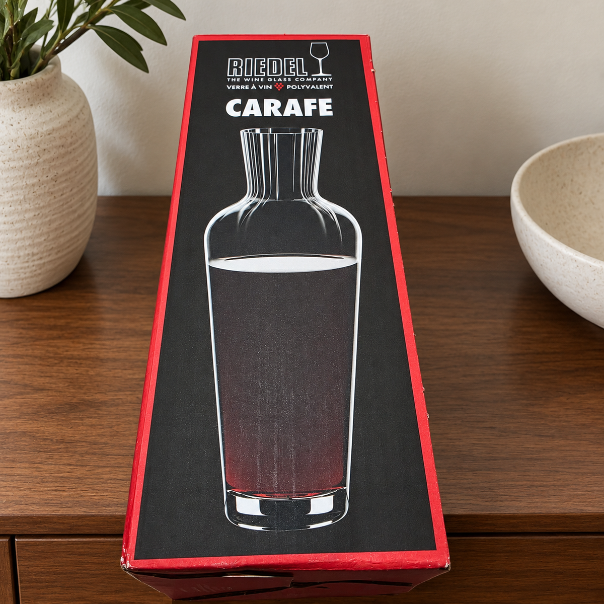 AI-generated lifestyle scene of one closed Riedel Wine Friendly carafe retail box on a cabinet shelf. Props not included.