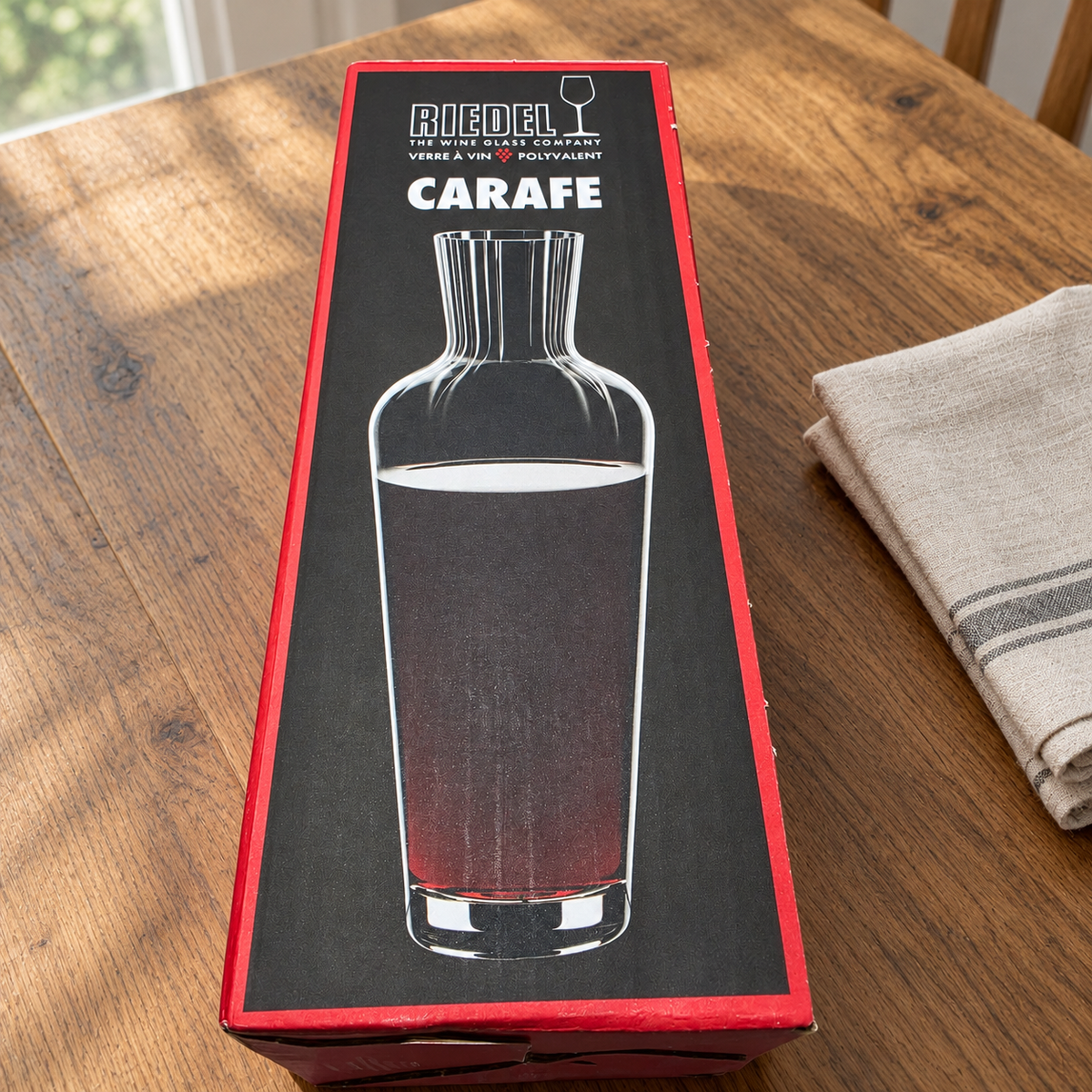 AI-generated lifestyle scene of one closed Riedel Wine Friendly carafe retail box on a dining table. Props not included.