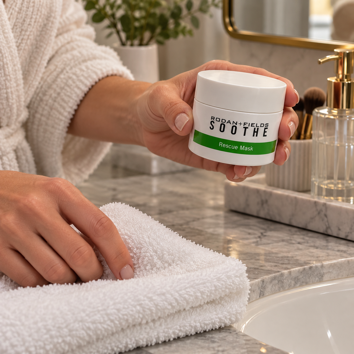 Holding a closed Rodan + Fields SOOTHE Rescue Mask jar beside a washcloth