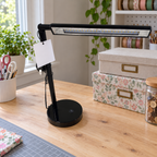 AI-generated lifestyle illustration of an unlit black Room and Retreat LED desk lamp in a craft table setting. Tag reverse shown; props not included.