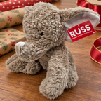 AI-generated lifestyle scene of the gray RUSS elephant plush with white trunk tip and attached red tag on a gift table. Props not included.