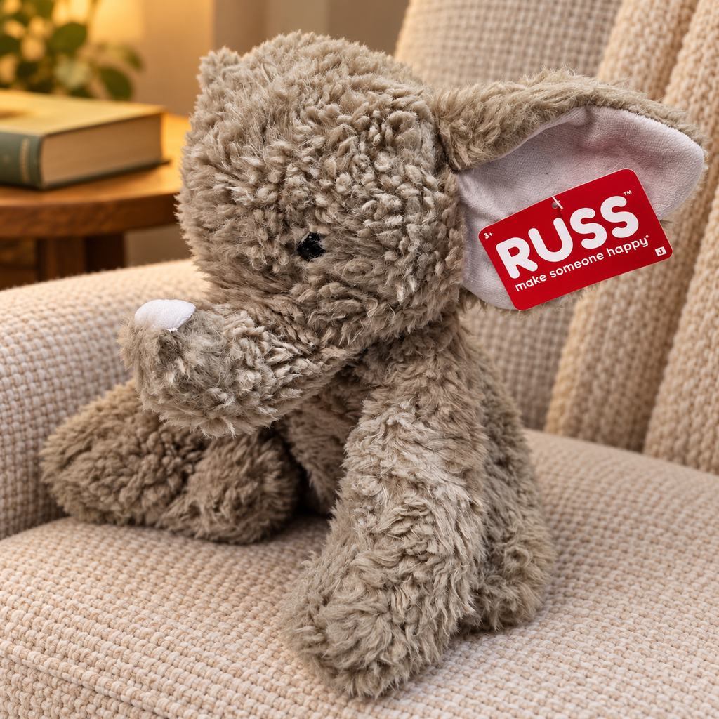 AI-generated lifestyle scene of the gray RUSS elephant plush with white trunk tip and attached red tag in a reading nook. Props not included.