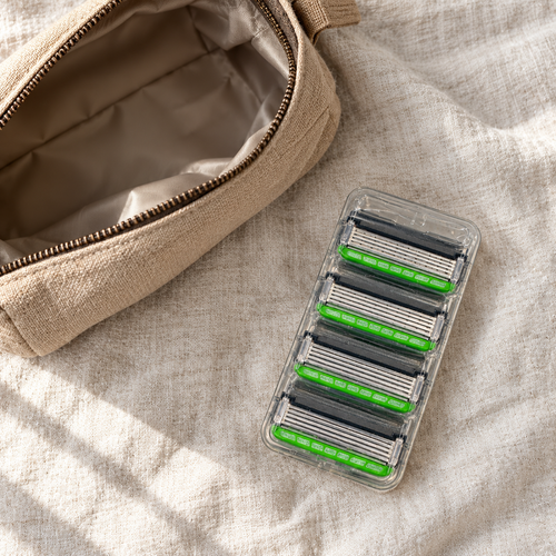 Four green Schick Hydro 5 refill cartridges in one clear tray beside an open toiletry pouch