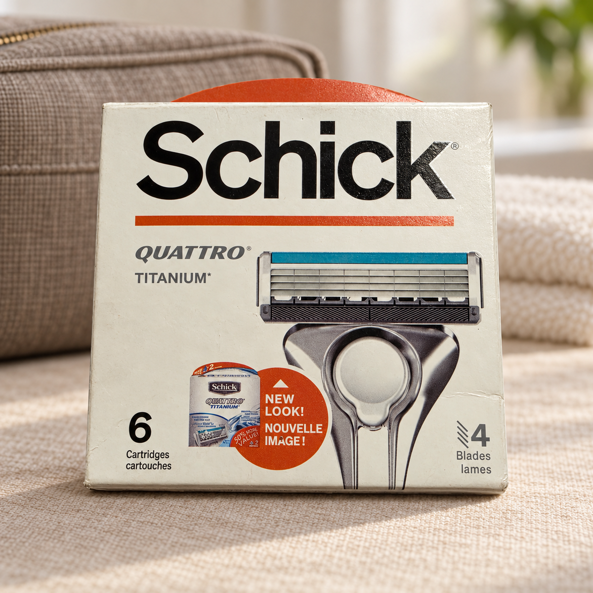 Illustrative lifestyle view of one Schick Quattro Titanium six-cartridge refill box beside a linen toiletry bag