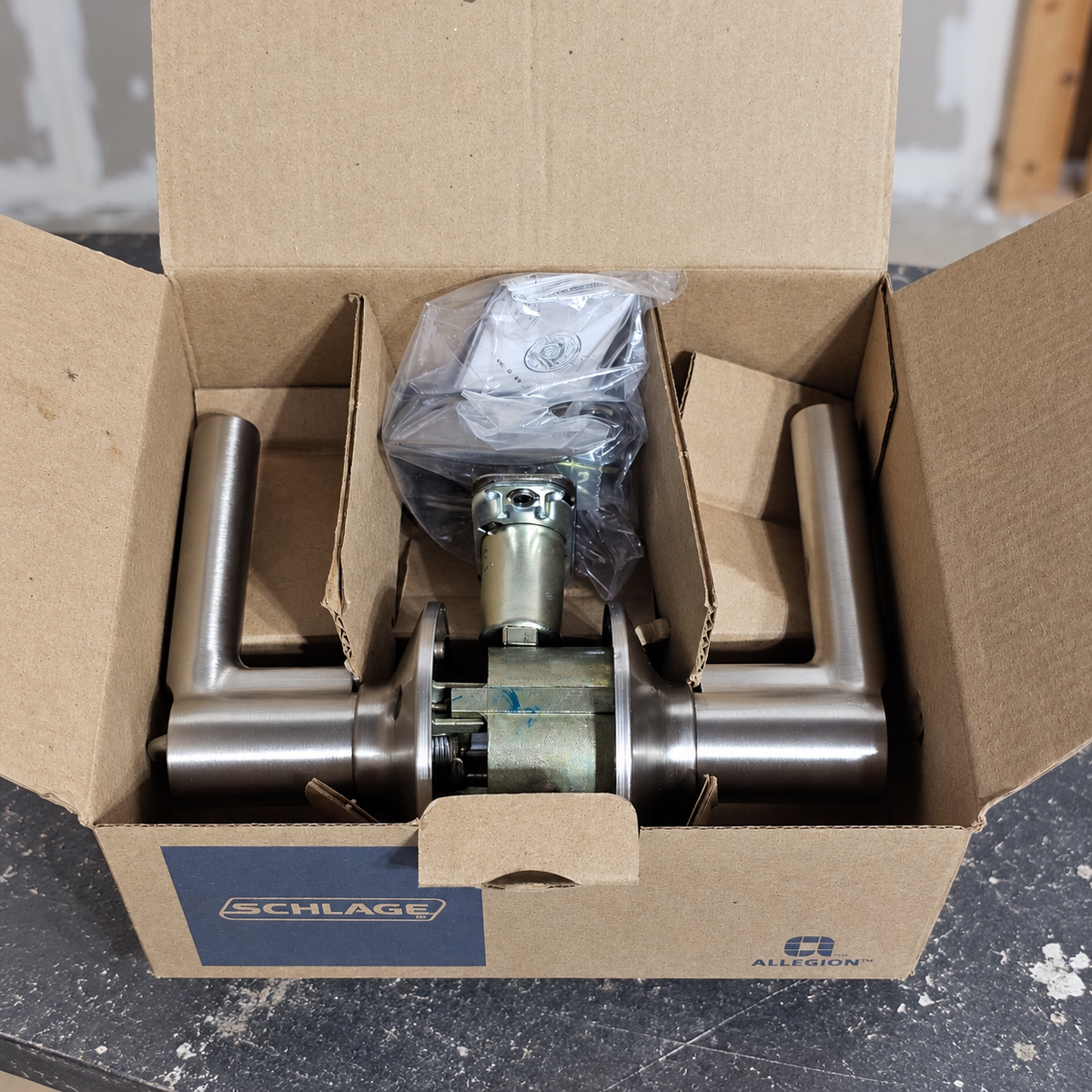 AI lifestyle illustration of the Schlage Broadway satin nickel lever set in its open box on a renovation workbench