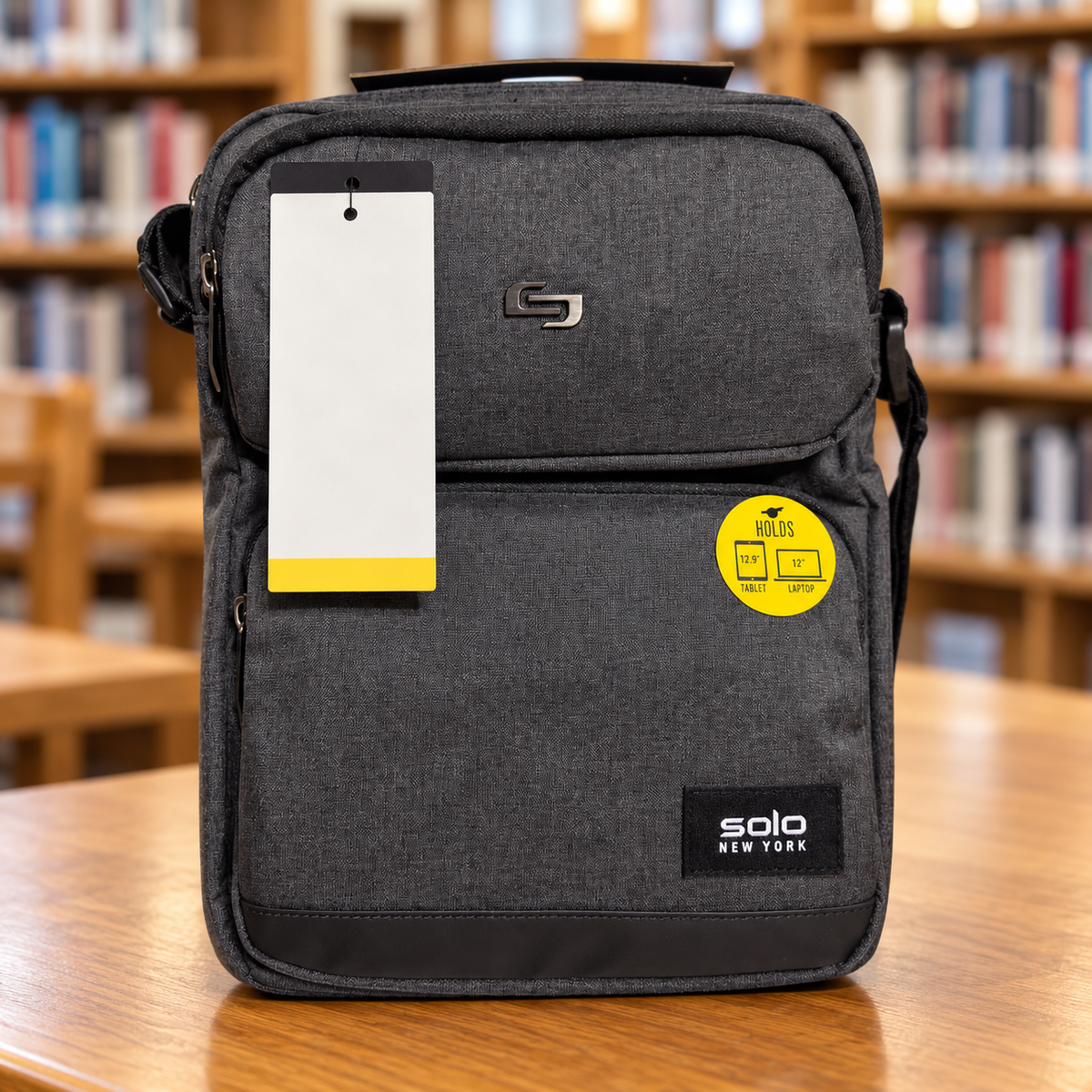 AI-generated lifestyle scene of the closed gray Solo New York Ludlow tablet sling on a library table. Props not included; hangtag shown from reverse.