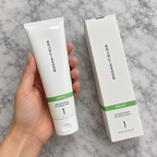 Overhead view of a hand holding the complete SOOTHE cleanser tube, showing its green label band and closed flip-cap beside the box.