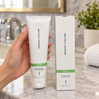 Hand holding a closed Rodan+Fields SOOTHE Calming Gel Cleanser tube, with its matching 125 mL box nearby.