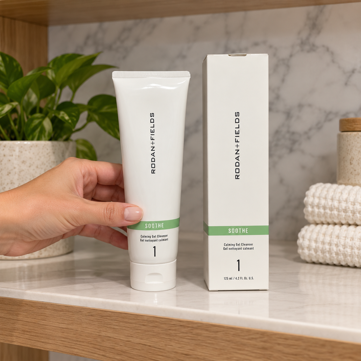 Hand placing a closed SOOTHE Calming Gel Cleanser tube on a dry bathroom shelf beside its matching box.