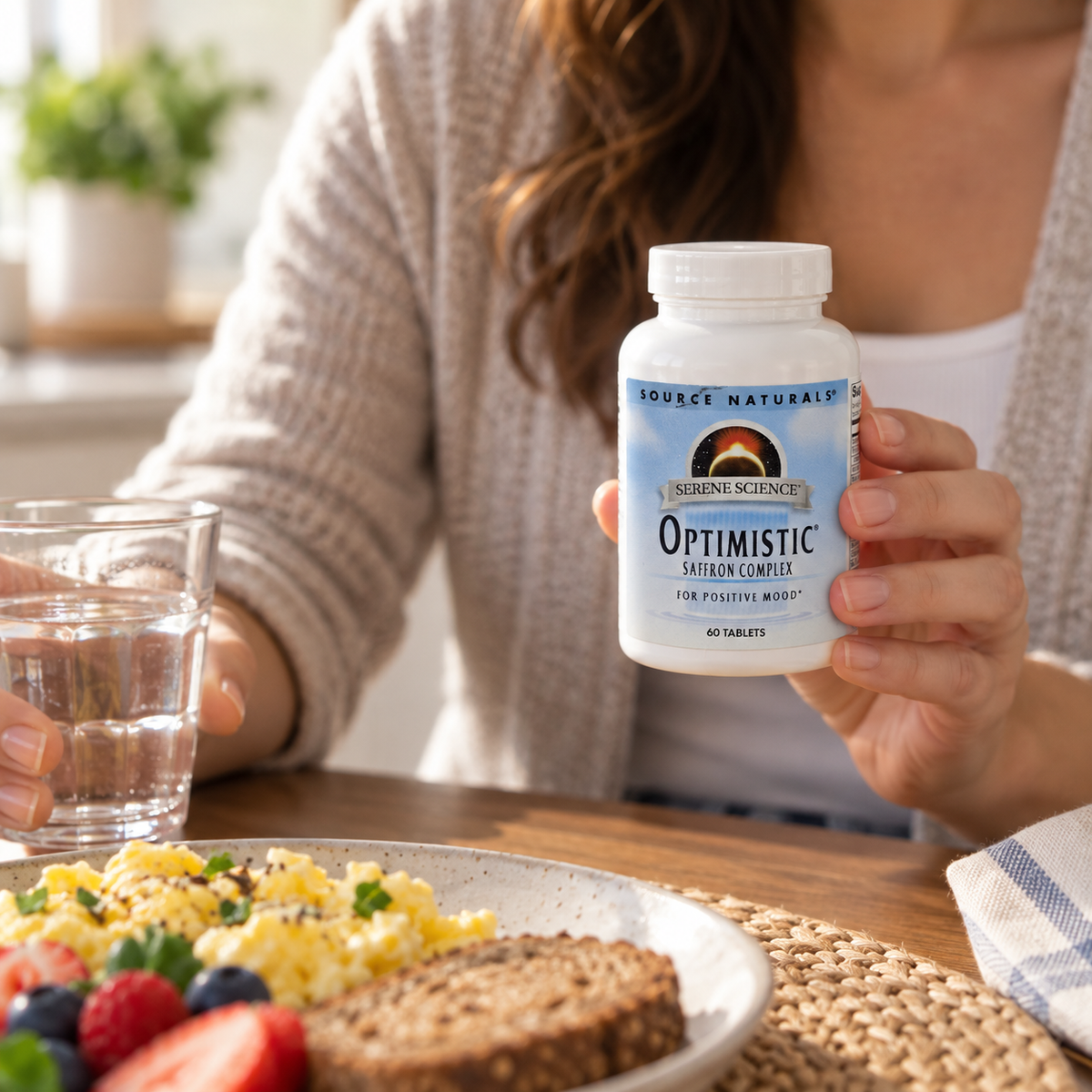 Source Naturals Optimistic 60-tablet bottle held beside breakfast and a glass of water