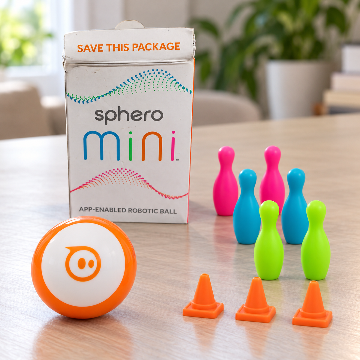 Orange and white Sphero Mini robot with three cones, six bowling pins and its retail box.