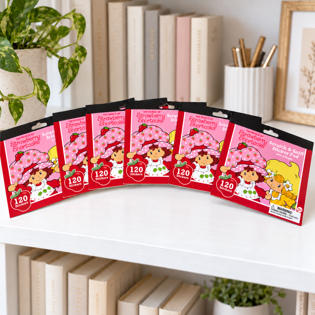 AI-generated lifestyle scene showing six closed Strawberry Shortcake scratch-and-sniff sticker pads,120 stickers per pad, on a stationery shelf. Props not included.