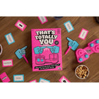That’s Totally You! game box, prompt cards, blue swivel hands and pink base arranged on a table.