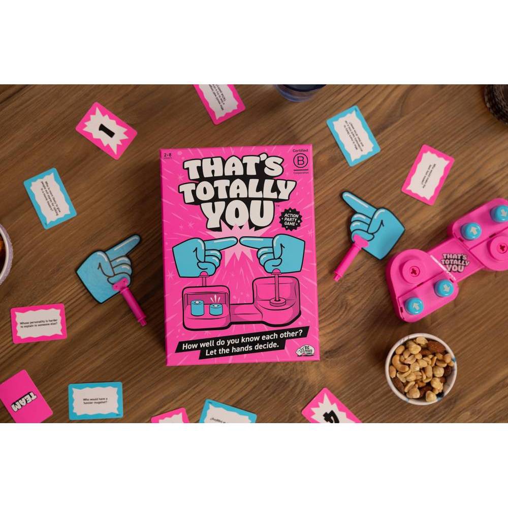 That’s Totally You! game box, prompt cards, blue swivel hands and pink base arranged on a table.