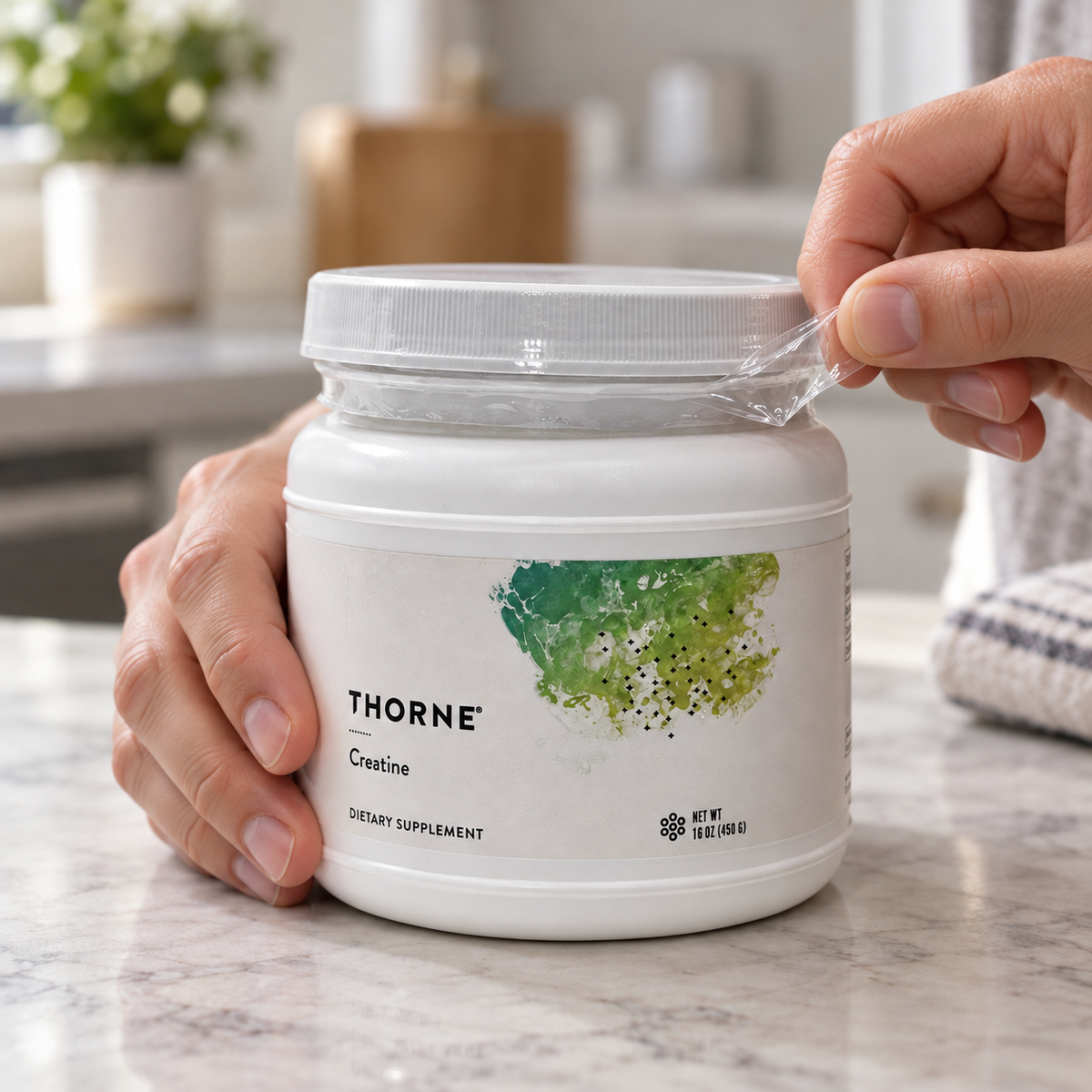 Illustrative adult hands peeling the clear outer neck band from a Thorne Creatine 450 g tub; the lid remains closed.