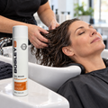 Stylist distributing conditioner through an adult client’s wet hair beside the older BosleyMD BosRevive Color Safe 300 mL bottle